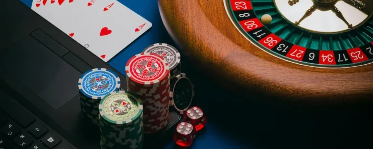 Roulette wheel, playing cards, chips, dice, and laptop for online gaming.